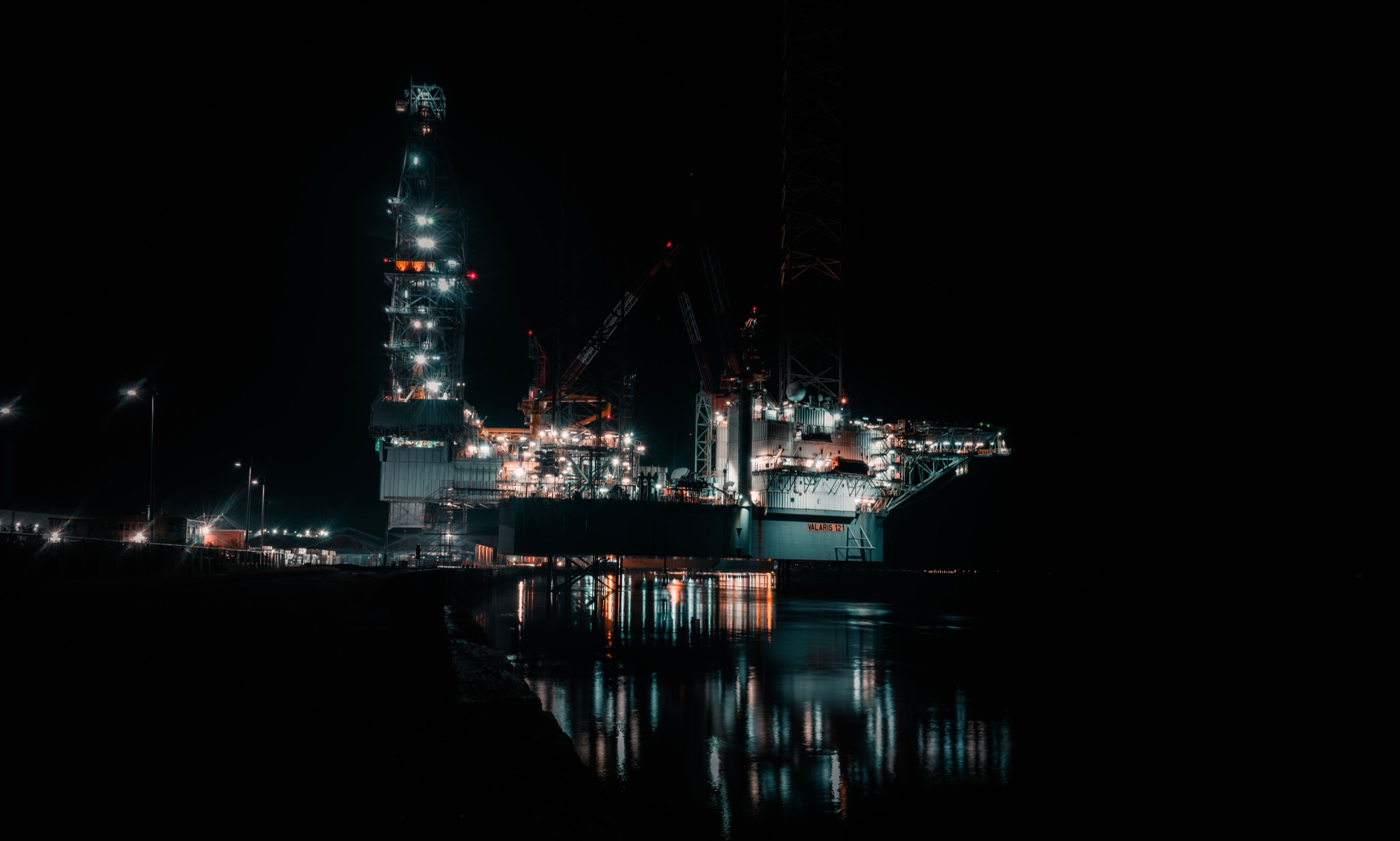 Jack-up drilling rig with illuminated derrick at night